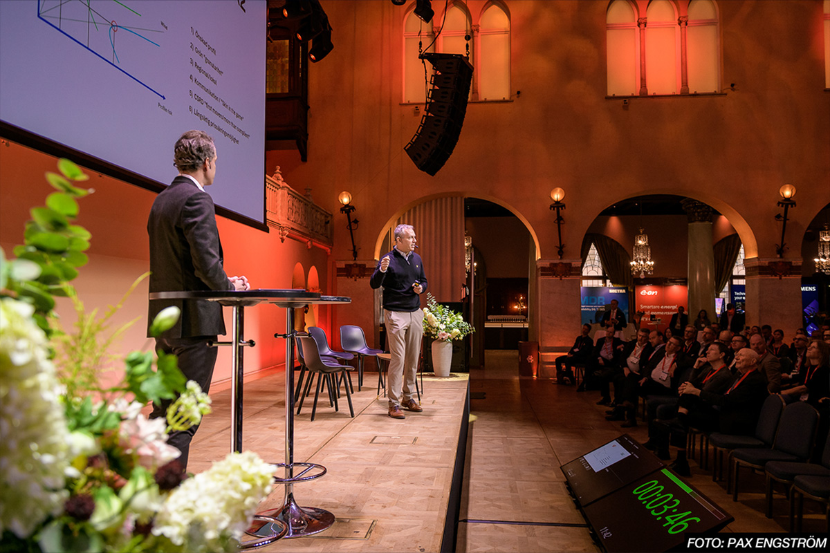 två personer står på en scen och pratar inför publik.