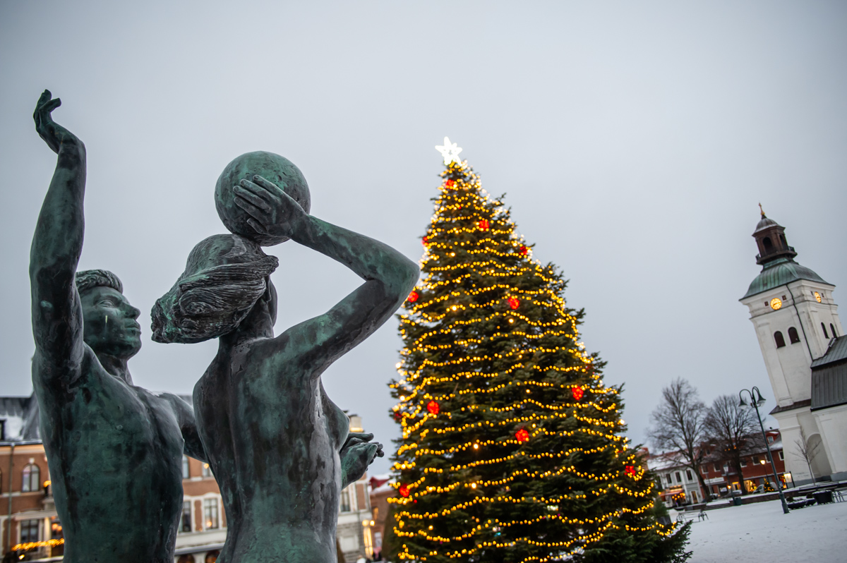 julgran med belysning på dagtid på ett torg med en staty framför